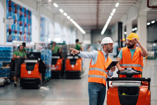 Warehouse workers discussing logistics and pointing with electric pallet jack