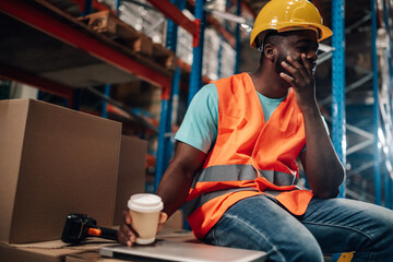 Tired warehouse worker taking a break with coffee