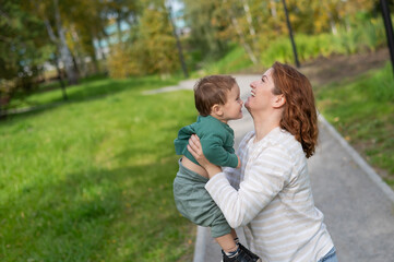 Fototapeta premium Caucasian woman holds her one-year-old son in her arms while walking in the park in autumn. 