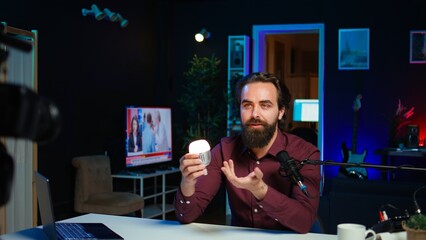 Smart light bulb used by tech specialist in studio to teach audience how to fix it, handheld camera shot. Focus on IoT home automation product held by media star, camera B