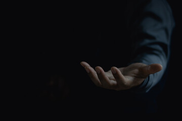A man is standing and holding an outstretched hand with an open palm. The businessman is presenting an empty hand isolated on black background. Give, receive, help, gesture, business present concept.