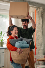 Happy couple carrying boxes and baskets while moving into new home