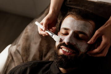 A beautician applies a scrub to the face of an older man in a spa, side light
