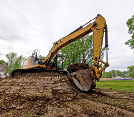 Fototapeta premium An industrial excavator, bulldozer or backhoe uses a hydraulic arm with a scoop to move dirt and grass in a field. City location with cloudy skies.