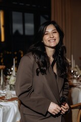 photo of a stylish brunette in an oversized pantsuit with a jacket against the background of a restaurant interior with blurred lights posing stylishly for a photo