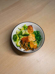 A rice bowl topped with grilled salmon, broccoli, mushroom, fish roe, and seaweed.