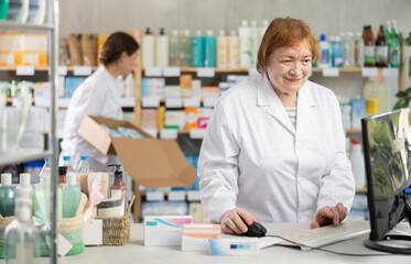 Obraz premium Elderly woman pharmacist working with computer in pharmacy