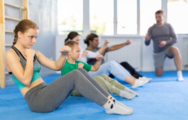 Obraz premium Concentrated girl, boy, woman, man at group training with trainer in gym practicing strikes in sitting position