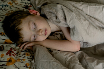 Obraz premium Little boy sleeping on a floral pillow and covered with a beige blanket. Cozy home concept.