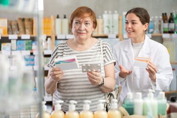 Qualified pharmacist helps a mature woman with the choice of paracetamol at the pharmacy