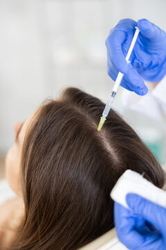 Young female patient lying on clinical chair undergoing hair care procedure by injection method