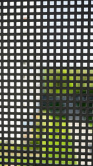 A close-up of a metal grid with square holes, isolated against a blurred outdoor background. Ideal...