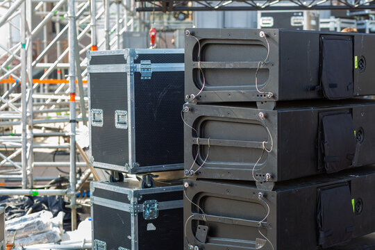 Stacks of sound equipment and lighting gear are arranged at an outdoor venue, ready for a concert.