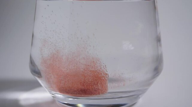 Effervescent tablets dropping into a glass of water slow motion on white background