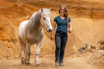 A young woman and her white icelandic horse gelding interacting in a sand pit; horsemanship concept