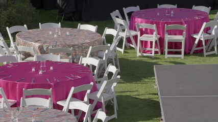 A smooth panning shot of empty outdoor banquet tables dressed in soft pink spring tablecloths. The scene suggests a peaceful moment before a celebration or event, with natural light.