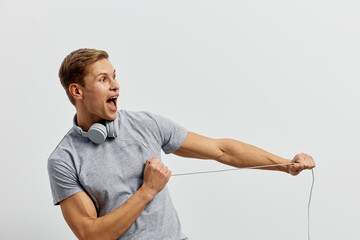 Energetic young man with headphones listens to music, enthusiastically singing and pulling a...