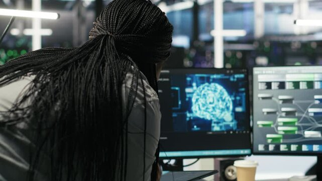 Data center engineer in wheelchair and colleague oversee automated tasks using node tree programming tool. Inclusive server farm team adjusts system settings based on AI analytics, camera B