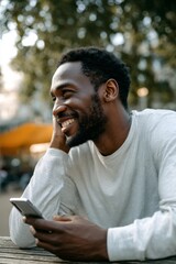 Fototapeta premium An attractive, smiling black man is holding his phone outdoors, looking joyful and relaxed.