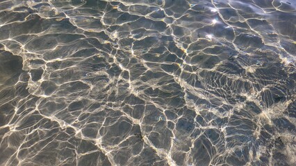 Sunlight reflects off rippling shallow water, creating shifting patterns of light and shadow on the sandy bottom.
