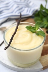 Tasty vanilla pudding, mint and pods on white table, closeup
