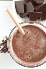 Tasty chocolate milk with shavings and pieces on white table, top view