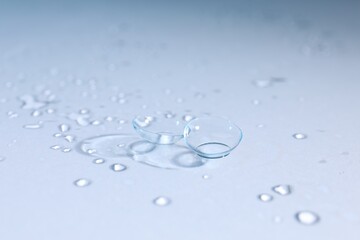 Pair of contact lenses and water drops on light mirror surface, closeup