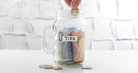 Woman putting money into tips jar at white table, closeup