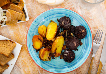 Delicious fried blood sausage served with potato slices and onions on plate