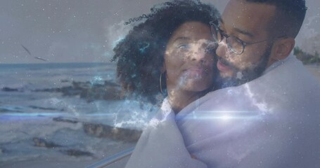 woman and man standing on coastal railing wrapping blanket, showing cosmic stars overlay for tech - Powered by Adobe