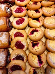 tempting variety baked goods is neatly arranged, featuring cookies with fruit fillings and sweet pastries. bright colors and textures make display appealing to customers. close up.