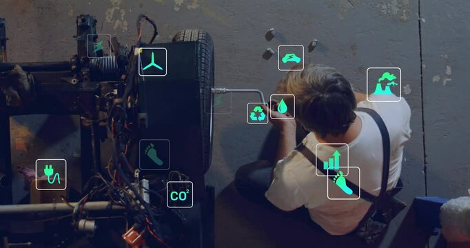 Mechanic working on chassis in automotive workshop, displaying green eco technology icons