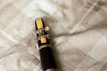 close-up of a clarinet mouth piece with a reed attached on a soft beige checkered blanket in natural window lighting 