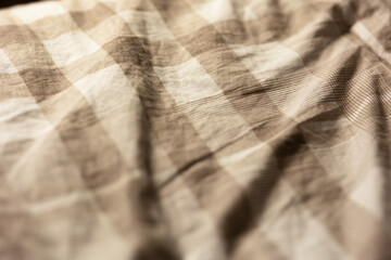 close-up of a soft slept-in comforter that is beige and checkered in soft moody lighting, image of a cozy blanket