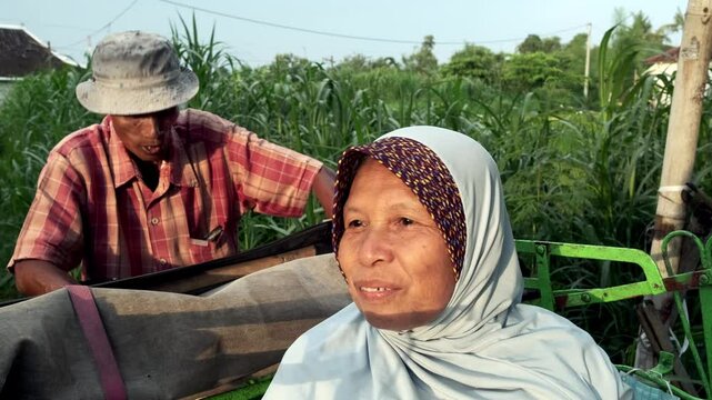 Becak driver chats in a relaxed and easygoing manner with his passenger, who is wearing a hijab, in a rural setting at sunset