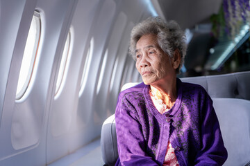 Senior Asian gray haired woman looking out the airplane window. Portrait of an elderly woman sitting in a window seat of an airplane