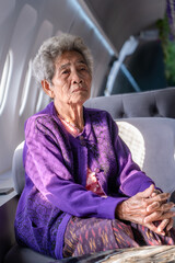 Senior Asian gray haired woman looking at camera. Portrait of an elderly woman sitting in a window seat of an airplane in cafe.