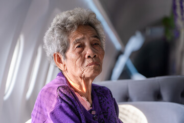 Senior Asian gray haired woman looking at sideways. Portrait of an elderly woman sitting in a window seat of an airplane in cafe.