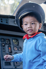 Boy child at controls of airplane sitting in cockpit wearing a pilot hat and sitting in an airplane cockpit, smiling confidently, portraying dreams of aviation and the future of flight.