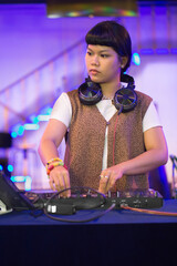 cool Asian female teen DJ's operating a turntable, capturing the essence of a live DJ performance at a club with headphones with a blurred background