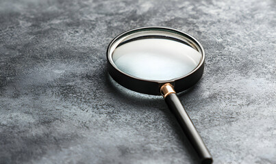 A magnifying glass rests on a mottled grey surface, with light reflecting on the glass and handle