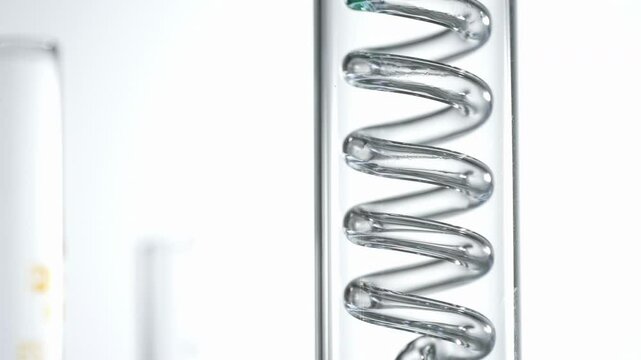 Close-up of the glass distiller in the experiment. Green oil flows in a spiral. Getting natural oil from natural substances concept. Perfect for Chemistry and Research Visuals