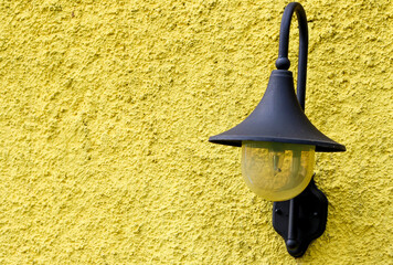 Black vintage wall lamp mounted on textured yellow wall in daylight.
