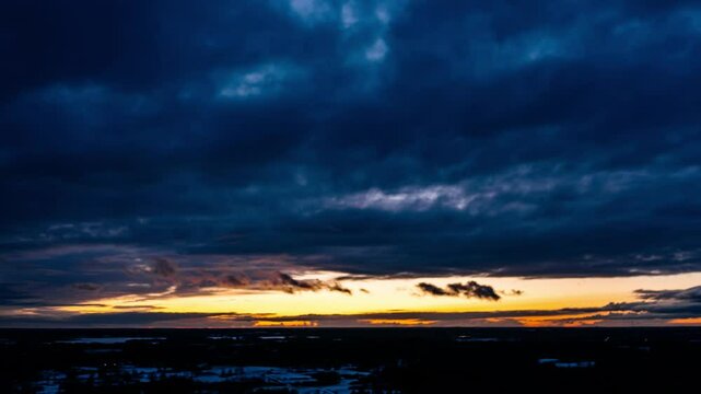 Aerial winter hyperlapse with dark clouds covering evening sunlight. Sunset behind clouds up in the air. Wide drone view of cloudscape in countryside.