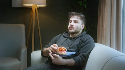 Man relaxing on a sofa while eating pizza at home in cozy evening light