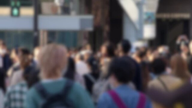 Blurred defocused view of scene unfolds as a multitude of individuals navigate their way through the iconic Shibuya Crossing in Japan. The group navigates through the busy city