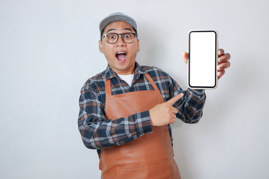 Surprised young Asian man barista barman employee wearing brown apron work in coffee shop using mobile phone isolated on white background. Small business startup concept