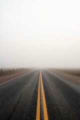 Fototapeta premium A deserted road stretching into dense fog, with a double yellow line fading into the mist.