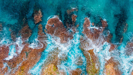 Aerial view of turquoise waves crashing on rocky coastline in vibrant tropical seascape.