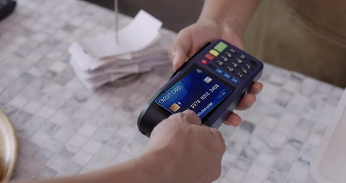 Hand inserting credit card into payment terminal during cafe checkout moment, slight wrist motion visible with fast-paced interaction at marble countertop near receipts and food tray